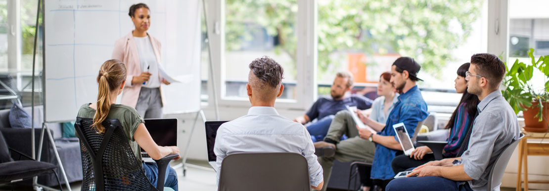 Eine junge Frau hält eine Präsentation vor dem multi-ethnischen Team in der Runde.