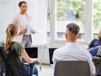 Eine junge Frau hält eine Präsentation vor dem multi-ethnischen Team in der Runde.