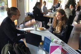 Das Foto zeigt Menschen an einem Infostand und Personen, die sie beraten.